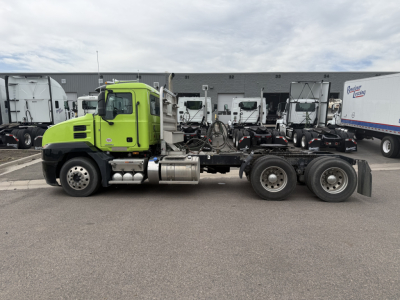 Truck chassis showing a lime-green Mack AN64T day cab with long wheelbase and dual rear axles, cab-forward design, side view in lot.