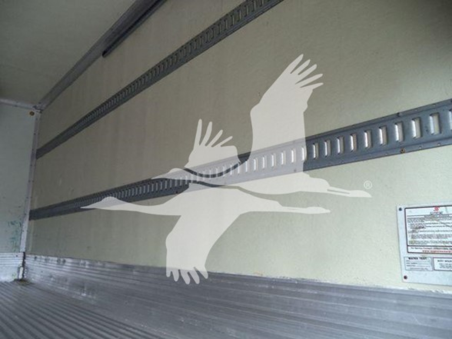 Interior wall of a refrigerated Isuzu truck trailer with a white bird graphic and metal rails. Small label plate visible on right side.