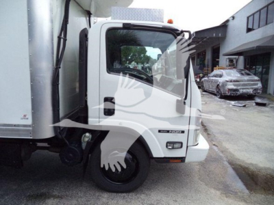 Isuzu NQR truck cab and side of refrigerated body with white exterior and black wheel; visible VIN plate area and window; urban backdrop