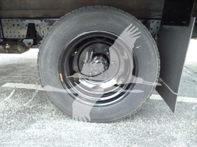 Wheel and tire of a refrigerated Isuzu NQR truck showing steel rim and tire with hub and undercarriage visible.