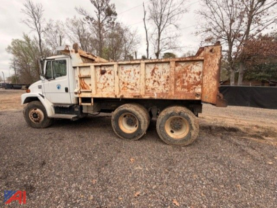 Dump truck side view showing 3-axle Freightliner FL80 with rusted dump bed and white cab.