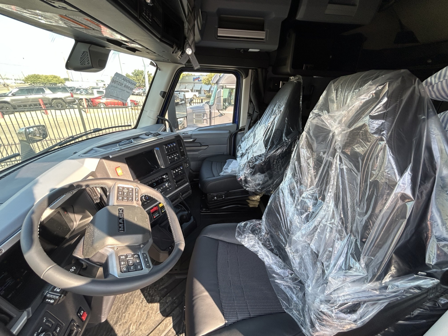 Cab interior of a new Mack PR64T76H truck showing steering wheel, dashboard, and stretched plastic-covered seats in the spacious cab.