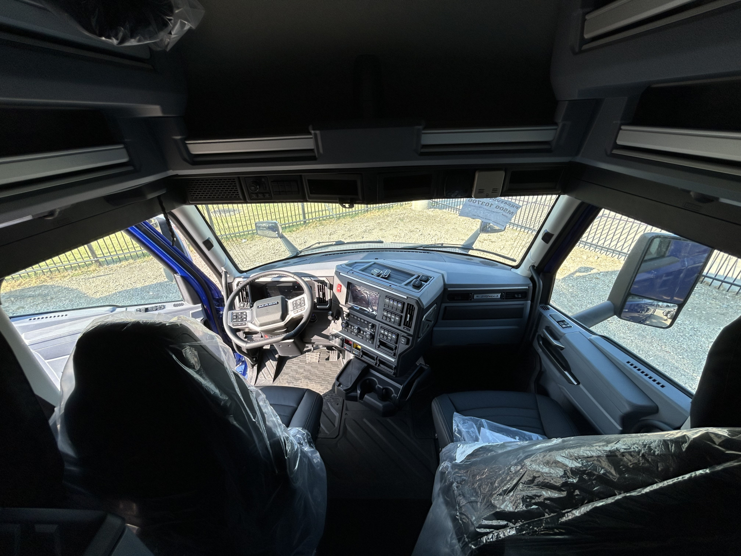 Truck cab interior dashboard view with steering wheel, dashboard controls, driver seat, and passenger seat; plastic protective covers on seats.