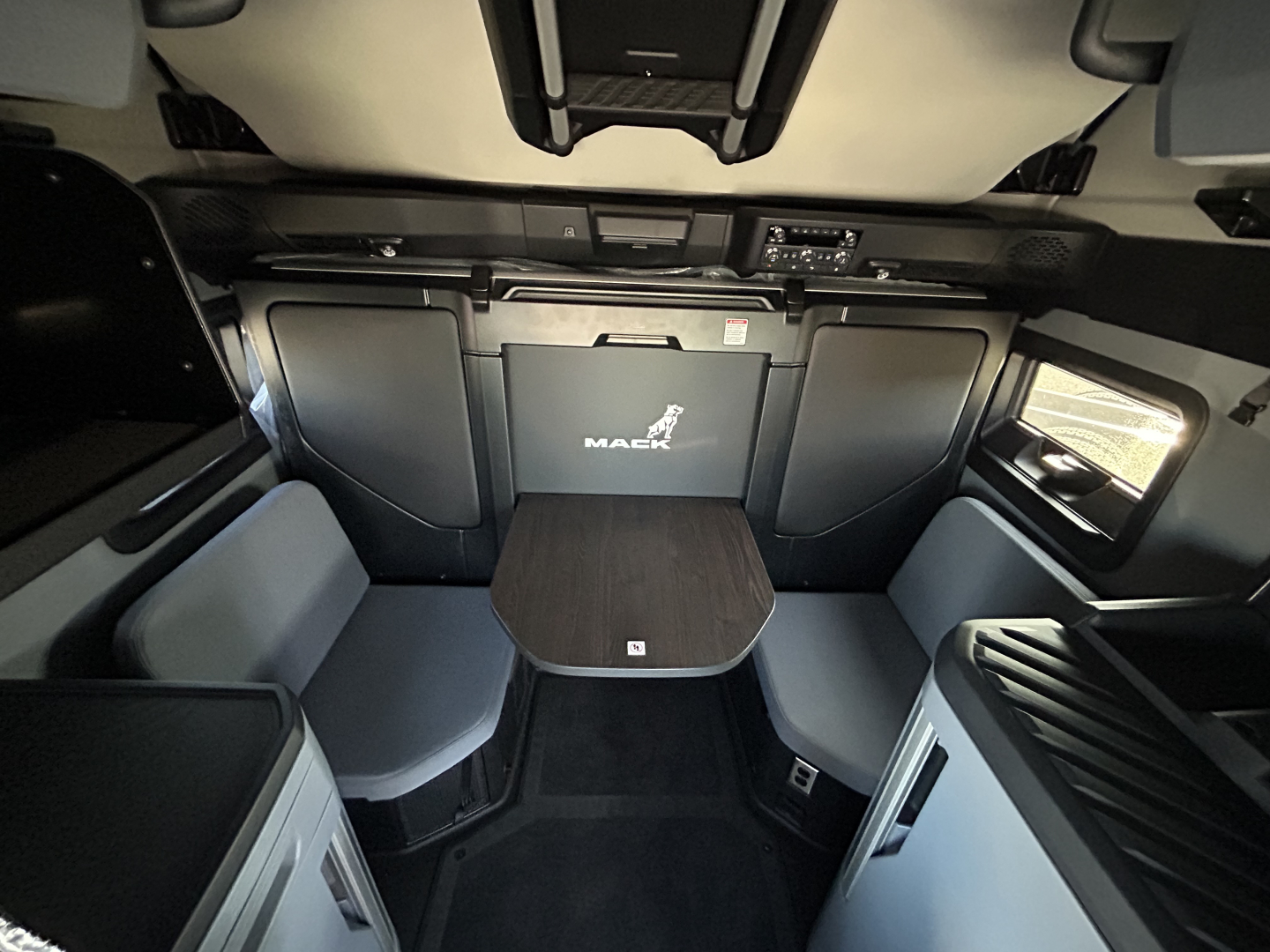 Cab interior of a 2027 Mack PR64T76H sleeper with seating area, table, and storage compartments visible.