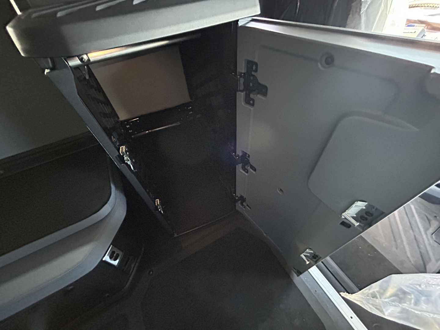 Interior cab storage area of a new 2027 Mack PR64T76H truck showing open cabinet with shelves and a door, dark gray interior, and a portion of the sleeper area.