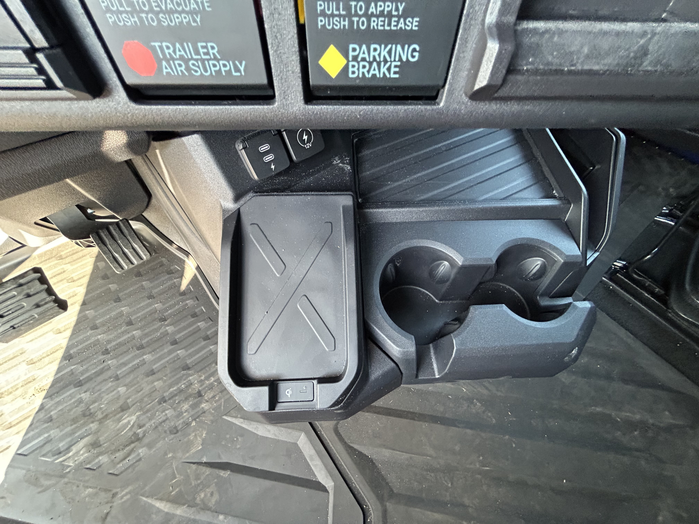 Truck cockpit area showing center console with cup holders and a rectangular device in view, with dash controls and buttons above.