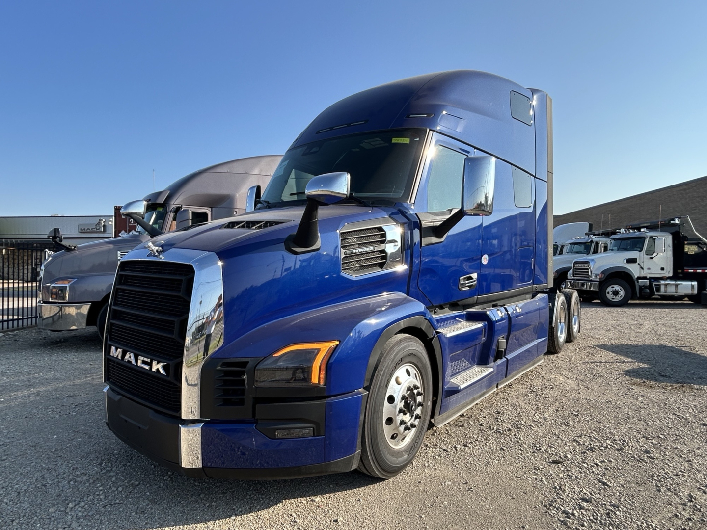 Truck front-left view of a blue 2027 Mack PR64T76H tractor in a dealership lot, showing cab, mirrors, and front grille.