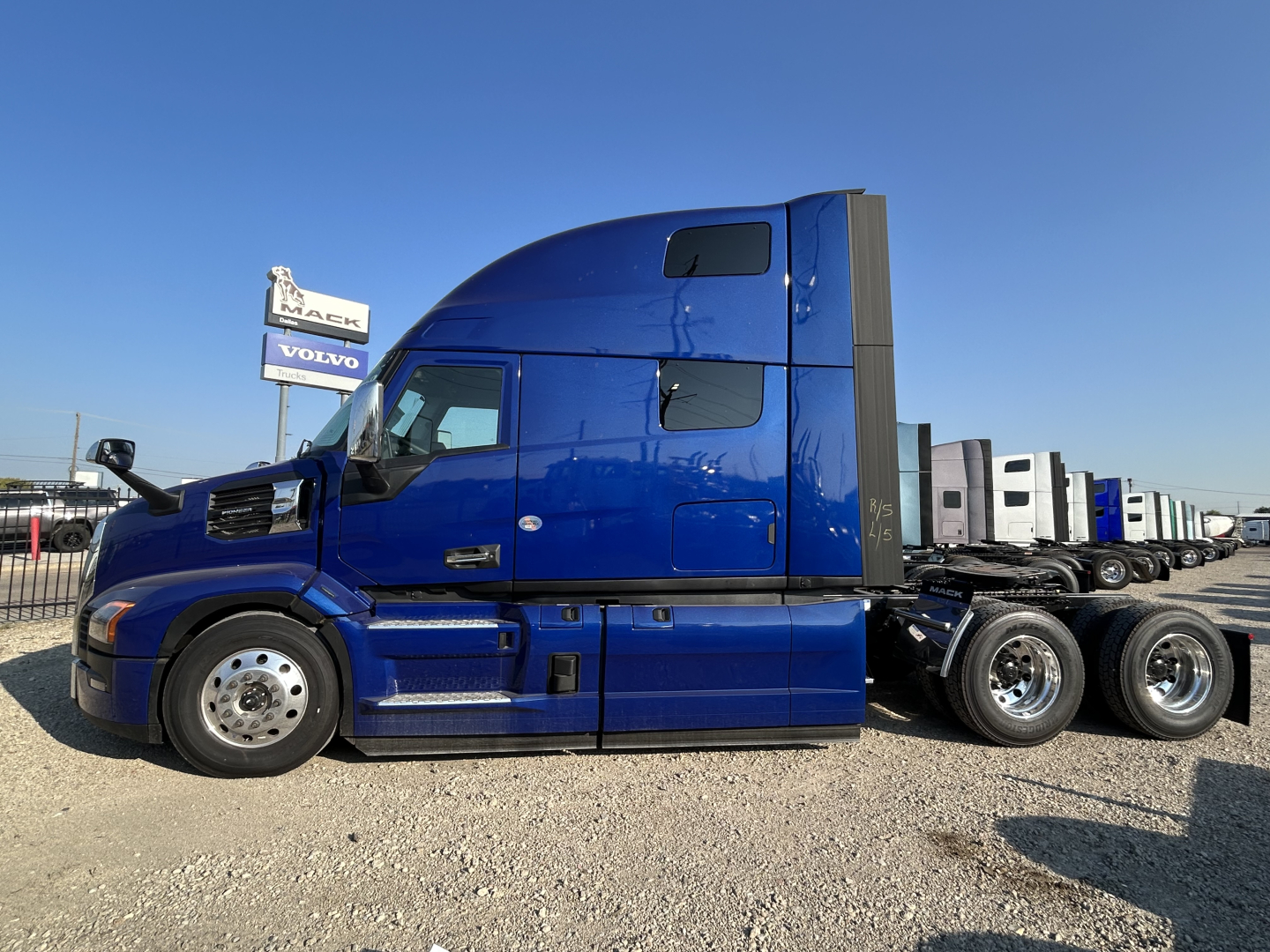 Truck side view of a blue 2027 Mack PR64T76H conventional sleeper with sleeper cab, multiple axles, and chrome wheels.