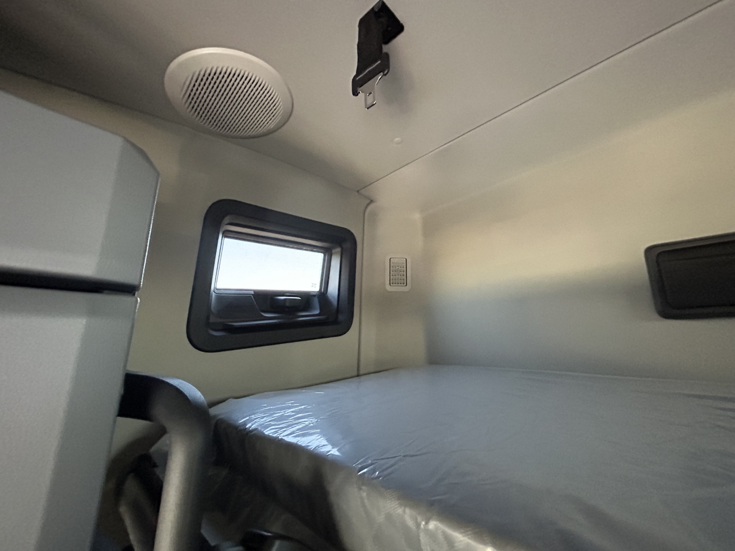 New Mack PR64T76H truck cab interior sleeper area with window, bed, and overhead storage.
