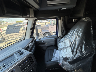 Cab interior of a 2027 Mack PR64T76H showing driver seat wrapped in plastic and dashboard controls visible.