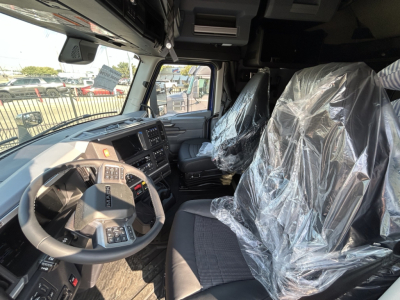Cab interior of a new Mack PR64T76H truck showing steering wheel, dashboard, and stretched plastic-covered seats in the spacious cab.