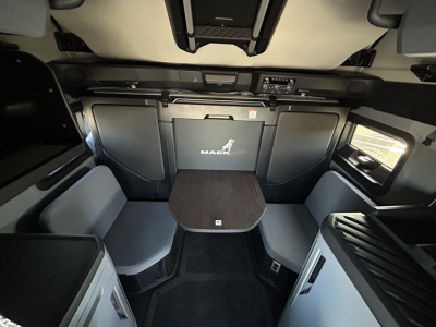 Cab interior of a 2027 Mack PR64T76H sleeper with seating area, table, and storage compartments visible.