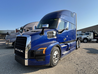 Truck front-left view of a blue 2027 Mack PR64T76H tractor in a dealership lot, showing cab, mirrors, and front grille.