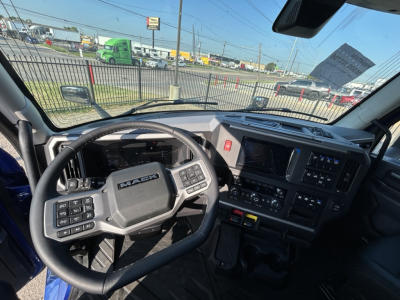 Interior view of a 2027 Mack PR64T76H truck cab from the driver’s seat, showing steering wheel, dashboard with touchscreen, and control panels.
