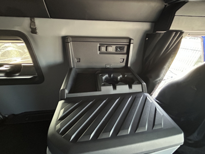 Truck cab interior showing storage console and side window with sunshade; control panel and cup holders visible.
