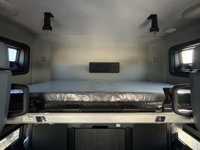 Truck cab sleeper bunk interior showing upper berth, storage panel, and restraints.