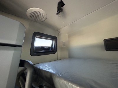 New Mack PR64T76H truck cab interior sleeper area with window, bed, and overhead storage.