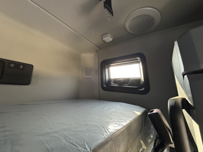 Mack PR64T76H sleeper cab interior showing bed area and window with speaker above.