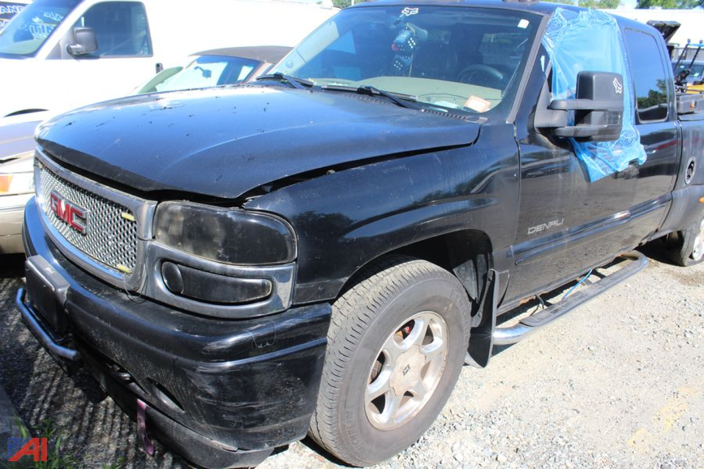 GMC Sierra 1500 extended cab pickup truck in black with front damage, passenger side door taped, blue tarp covering rear windows, parked on gravel