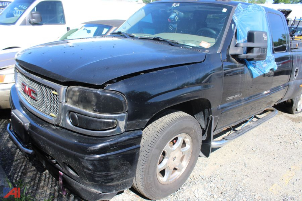 GMC Sierra 1500 extended cab pickup truck in black with front damage, passenger side door taped, blue tarp covering rear windows, parked on gravel