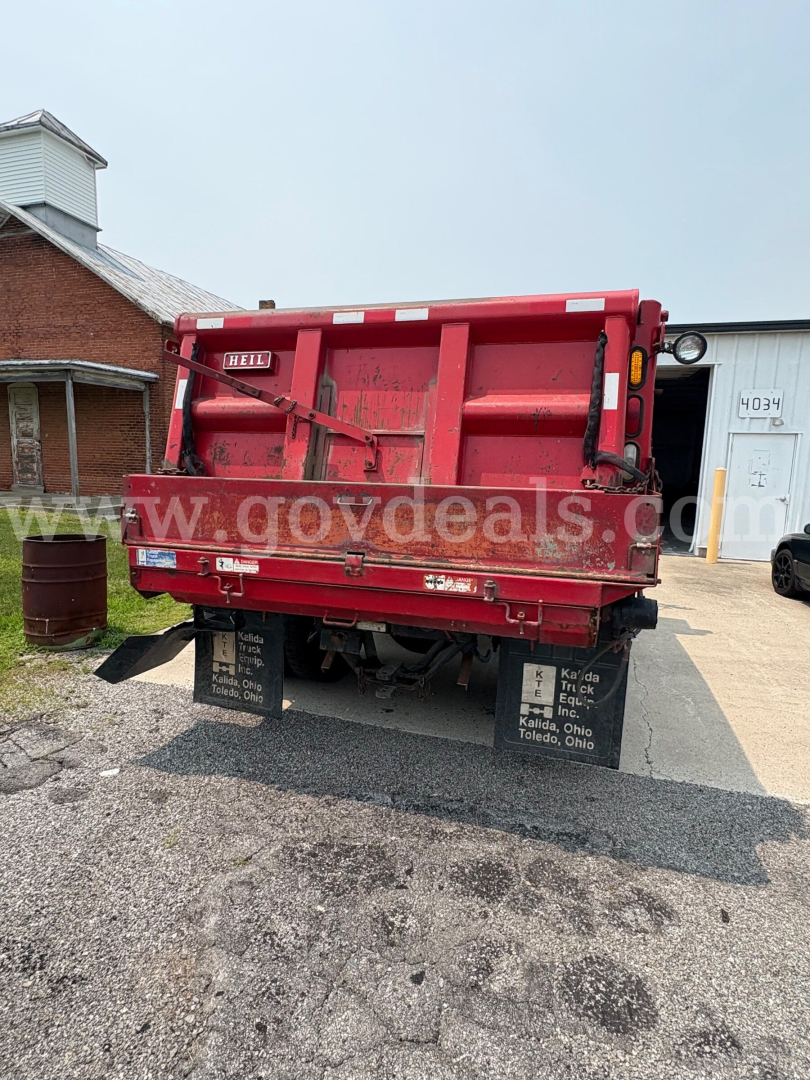 Dump truck rear showing red dump bed with black undercarriage and mud flaps; various white and black warning stickers visible; watermark across image from govdeals.com.