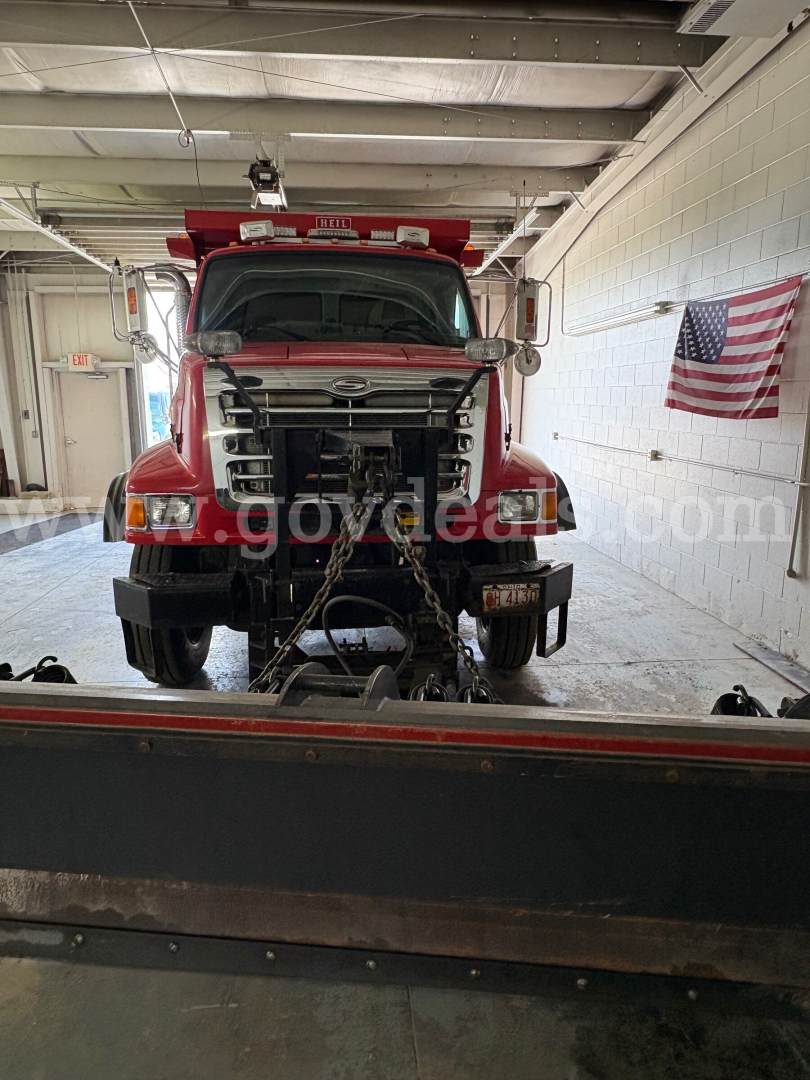Front view of a red 2004 Sterling L7500 dump truck in a workshop, with chain bindings on the front and an American flag on the wall.