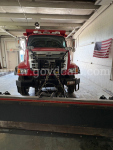 Front view of a red 2004 Sterling L7500 dump truck in a workshop, with chain bindings on the front and an American flag on the wall.