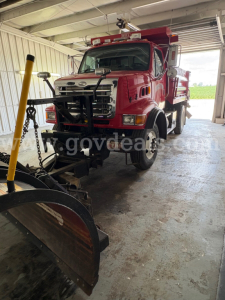 Dump truck chassis showing front grille and mounted snowplow equipment and red Sterling L7500 body with warning lights