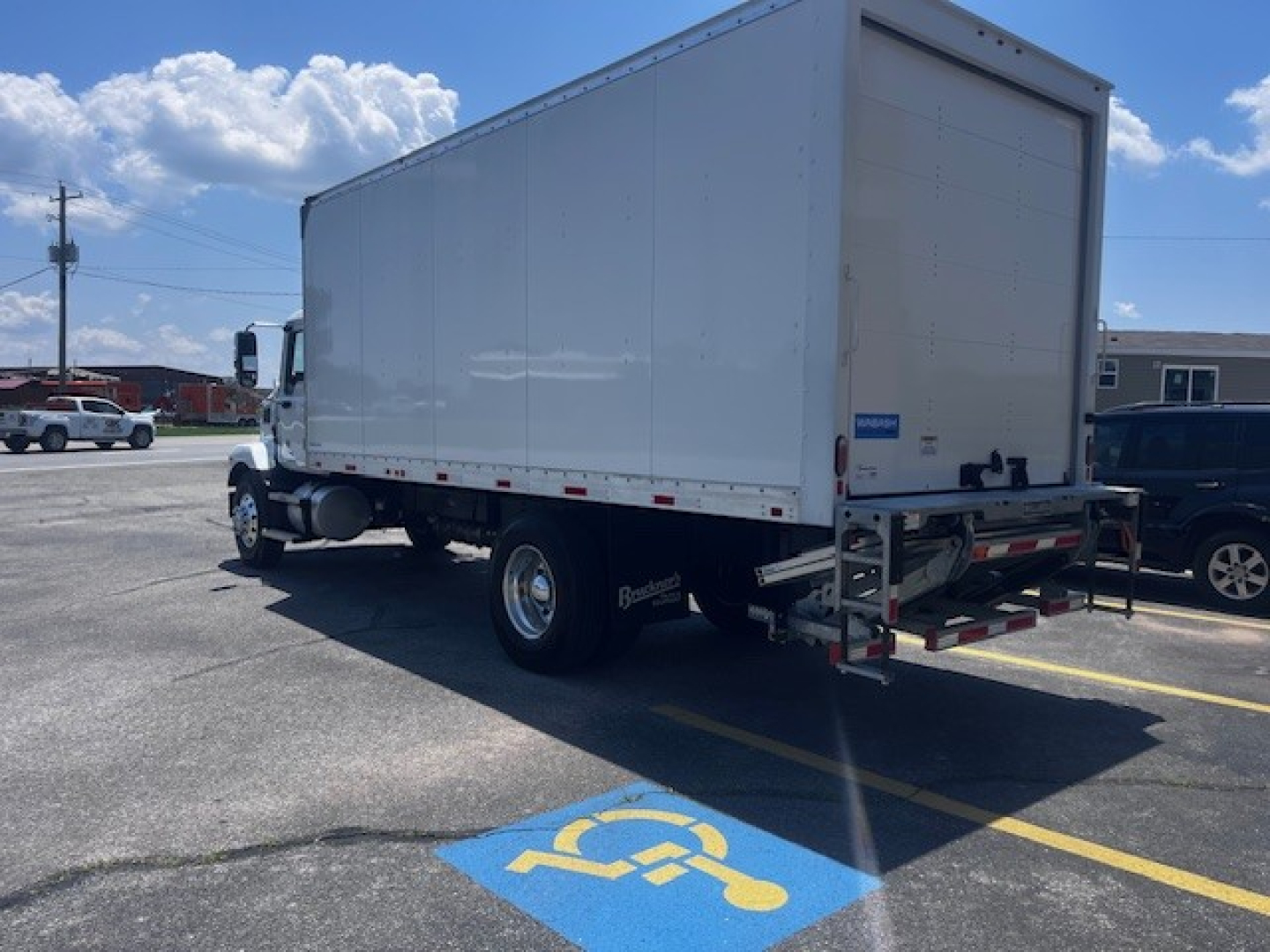 Box truck rear/side view showing cargo box and chassis on a 2025 Mack MD6, white box body, dual rear wheels, rear underride guard, blue sky.