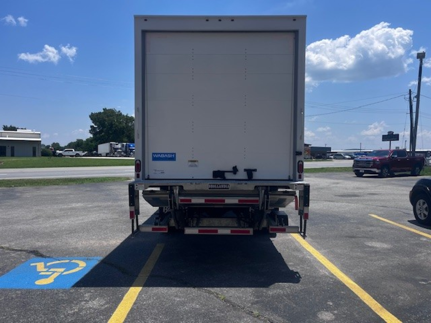 Rear view of a new Mack MD6 box truck showing the back doors and bumper with reflective tape.