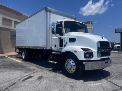 Mack MD6 box truck in white, three-axle cab with cargo box, front chrome bumper, large mirrors, and black grille. Clear sky.