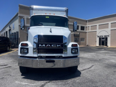 Front view of a white 2025 Mack MD6 box truck showing bold Mack grille, chrome bumper, and large side mirrors in a dealership lot.