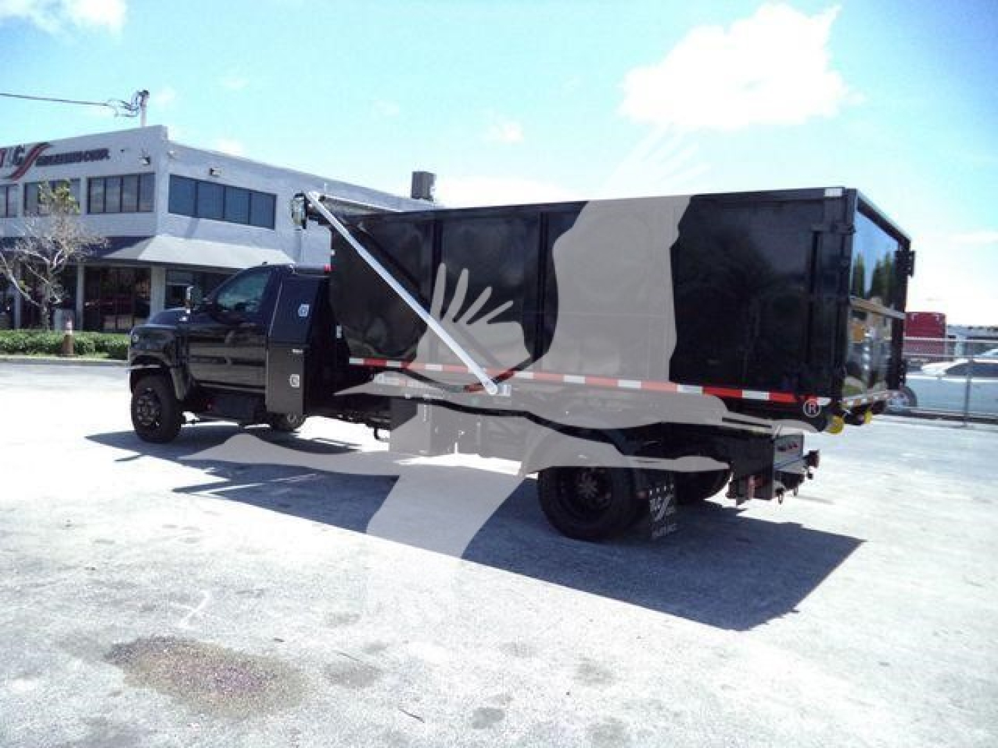 Truck with a large black dump body in a parking lot. Side graphics show an eagle-like white silhouette. No visible serial numbers or labels readable on the truck from this angle.