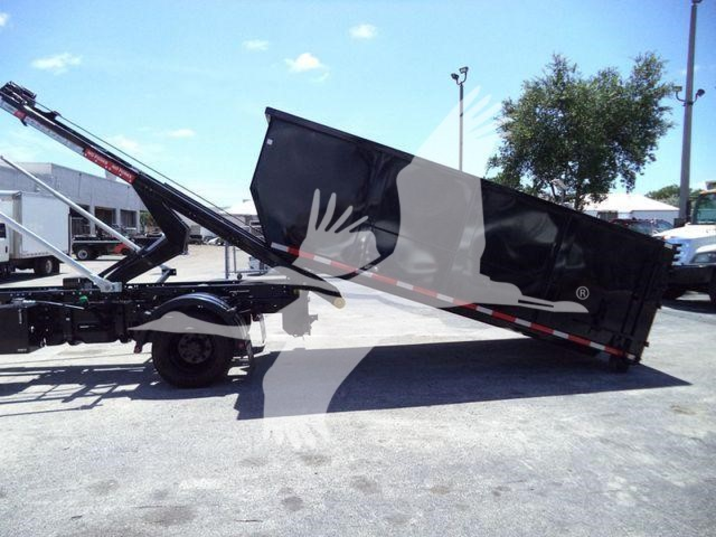 Truck-mounted rollback trailer showing hydraulic lift with black dump bed and shoulder with safety rails.