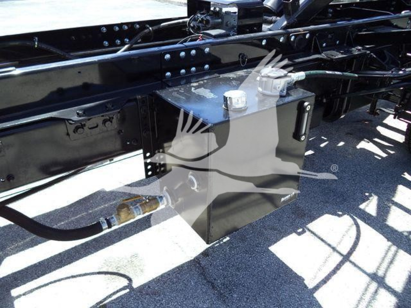 Intermodal truck chassis showing a gray rectangular toolbox mounted under the frame with a white cap on top and hydraulic line nearby.