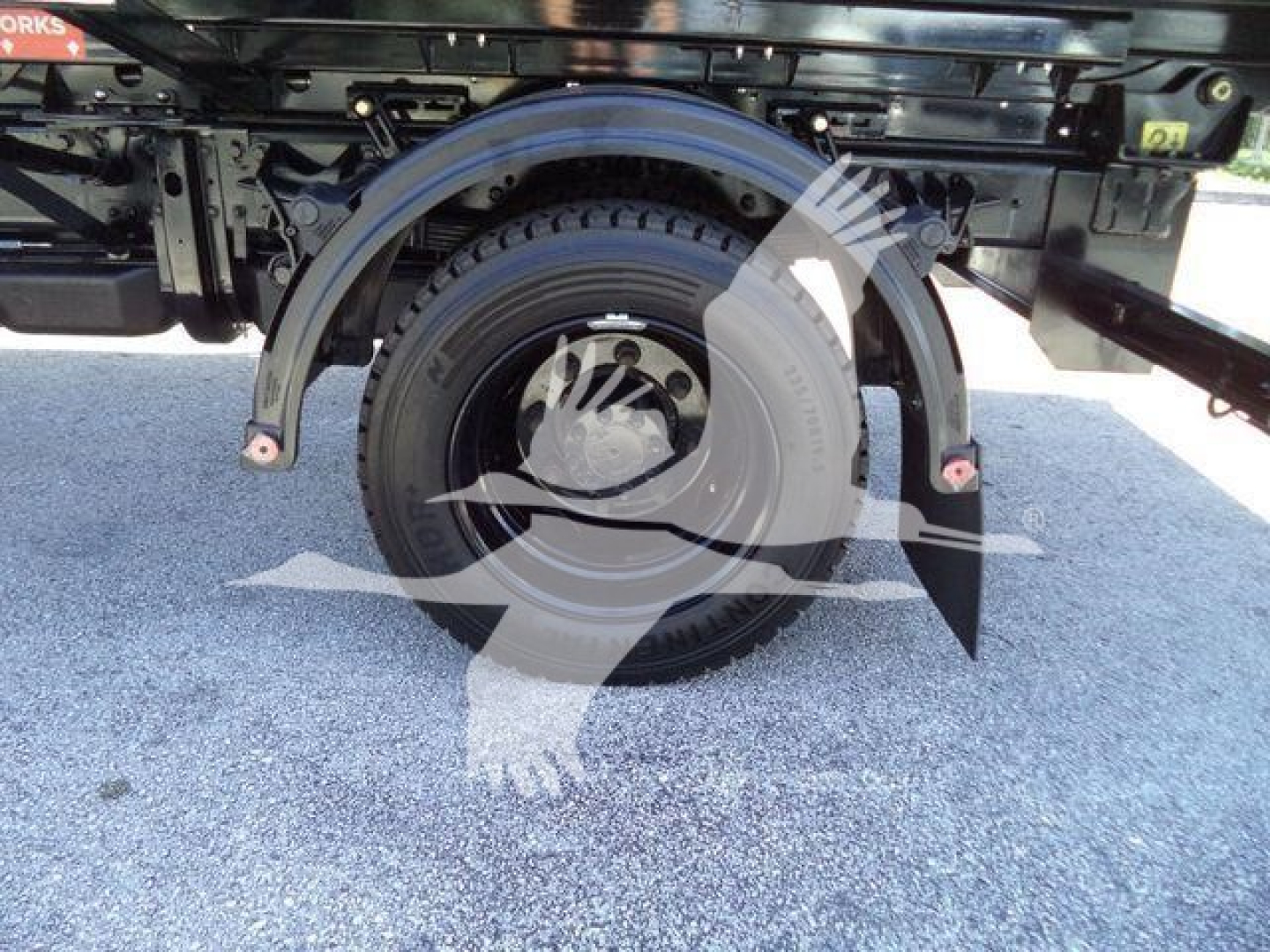 New truck with wheel-well and spare tire visible underframe; partial text on the truck bed and wheel arch; no engine or fluid labels readable.