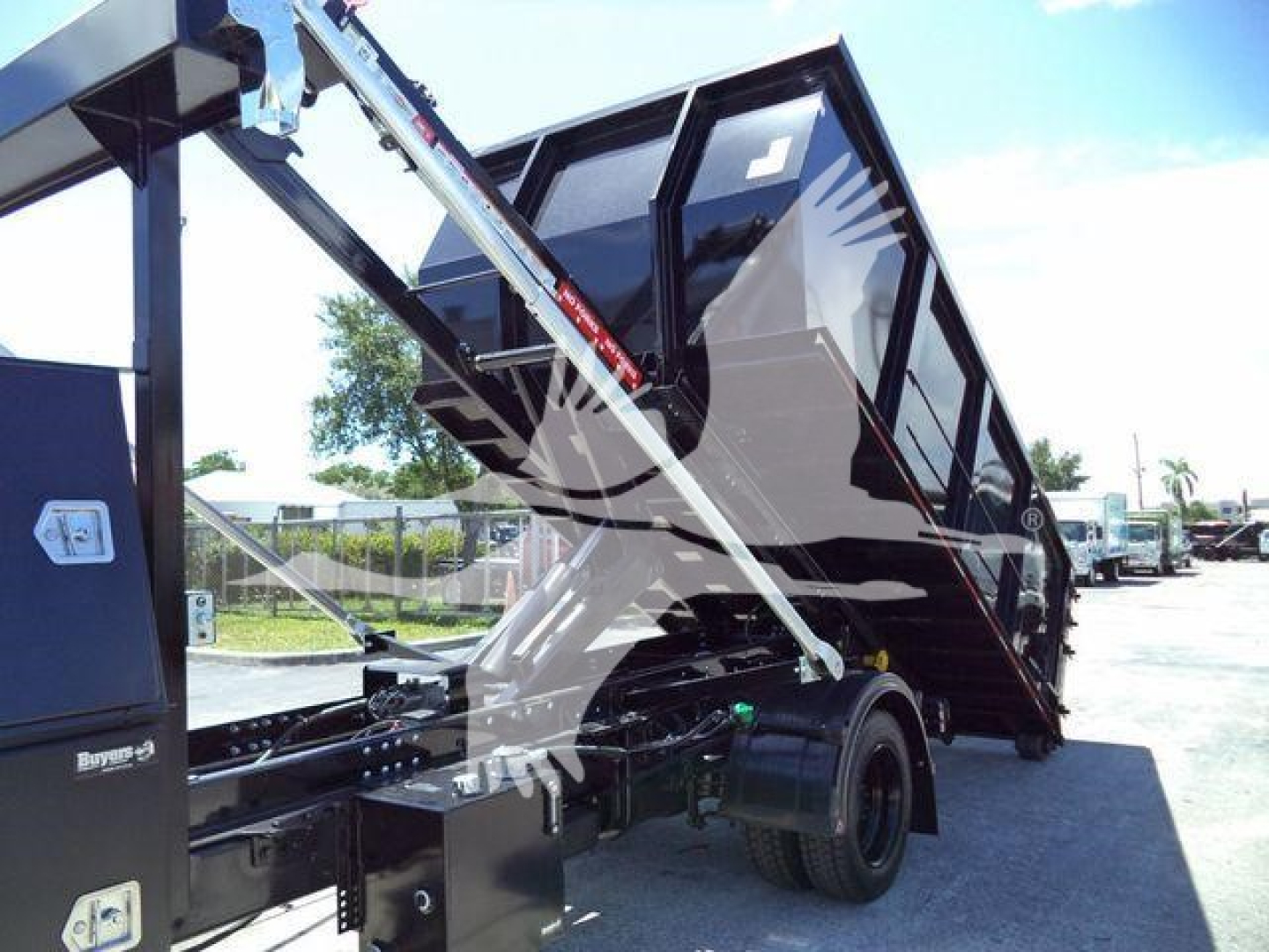 Dump truck bed and hydraulic lifting mechanism showing a black dump body tilted for unloading with glass cab and side rails visible.