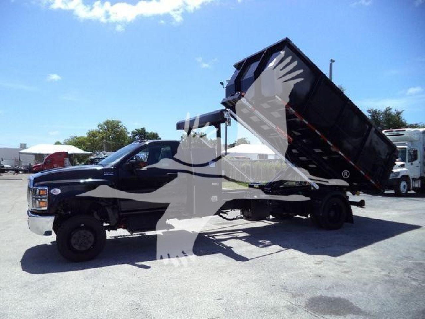 Truck with a raised dump bed in a lot. Side view of 2023 International CV roll-off truck with hydraulic hoist and black/gray cab.