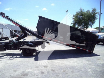 Truck-mounted rollback trailer showing hydraulic lift with black dump bed and shoulder with safety rails.