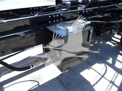 Intermodal truck chassis showing a gray rectangular toolbox mounted under the frame with a white cap on top and hydraulic line nearby.