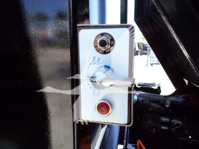Panel with red emergency stop button and control knob, white faceplate mounted on a black surface, with hydraulic lever and text around the knob.
