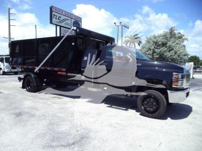 Dump truck in service with black dump body and extended cab, showing CV515REG14SNG1 stock number; roll-off truck in dealership lot.