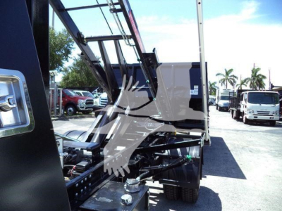 Trucks and equipment in a lot showing a black International CV roll-off with hydraulic arms and exposed engine area.