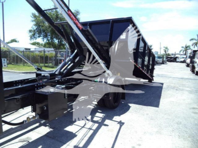 Loader truck bed in profile showing rolloff dump with hydraulic arms and black chassis. Side view of cargo container on trailer with wheels visible.