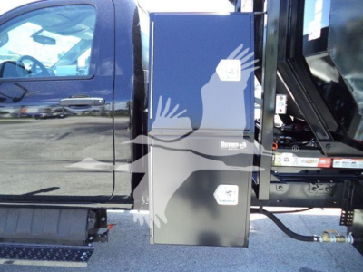 Truck cab side with vertical toolbox and hydraulic lines; label text not fully legible but shows storage box mounted between cab and bed.
