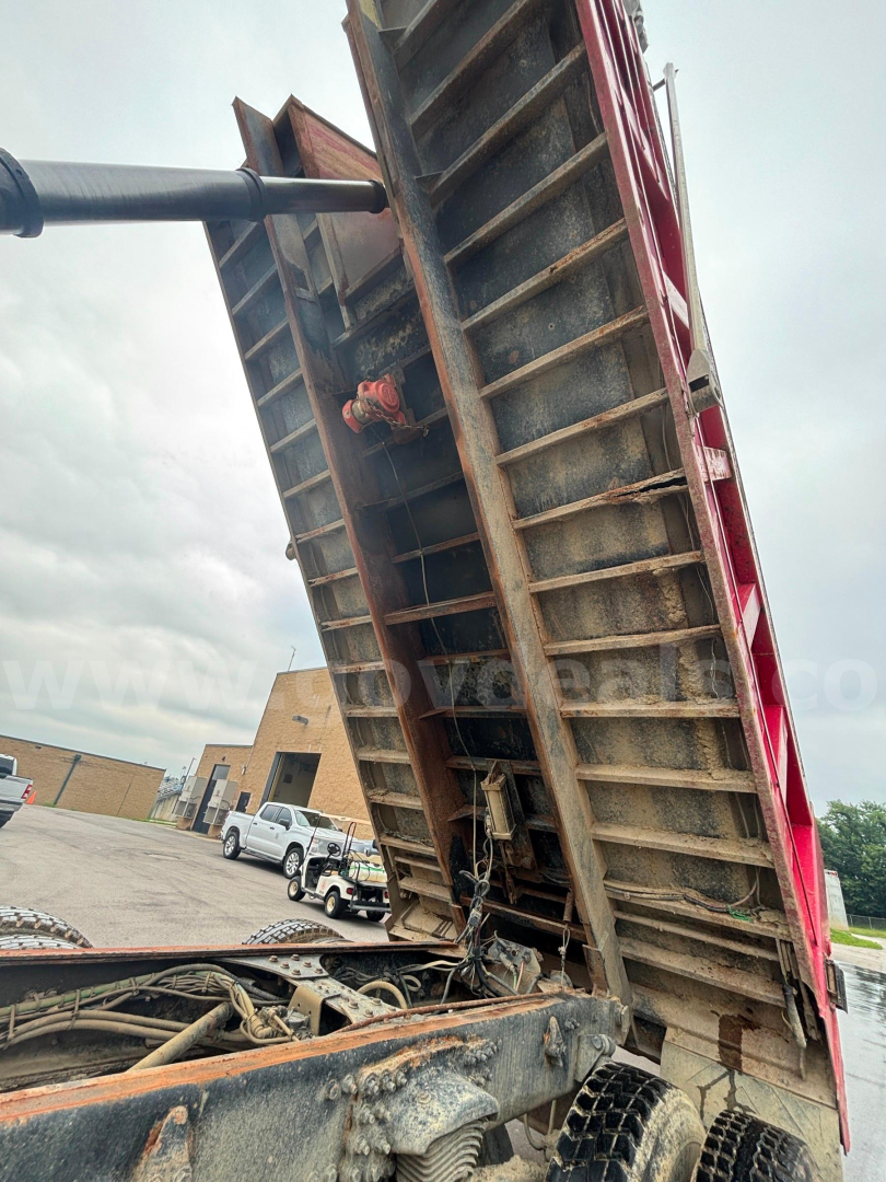 Dump truck bed tilted up showing metal scissor lift mechanism and hydraulic cylinder with visible rust and components.