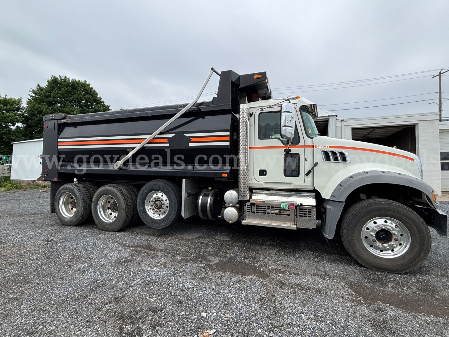 Mack Granite dump truck in service view showing black dump body with orange reflective stripe and white cab, side of truck with multiple axles and chrome steps.