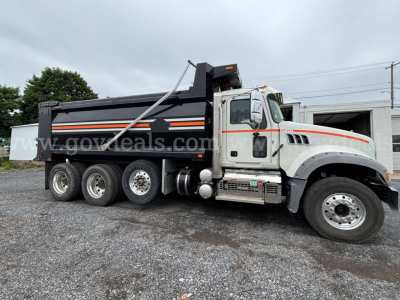 Mack Granite dump truck in service view showing black dump body with orange reflective stripe and white cab, side of truck with multiple axles and chrome steps.