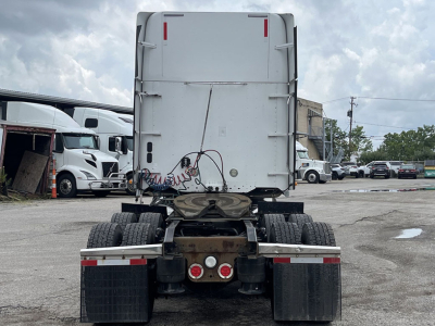 Rear view of a Freightliner Coronado truck chassis with dual rear axles and mud flaps; some wiring and components visible under the sleeper cab.