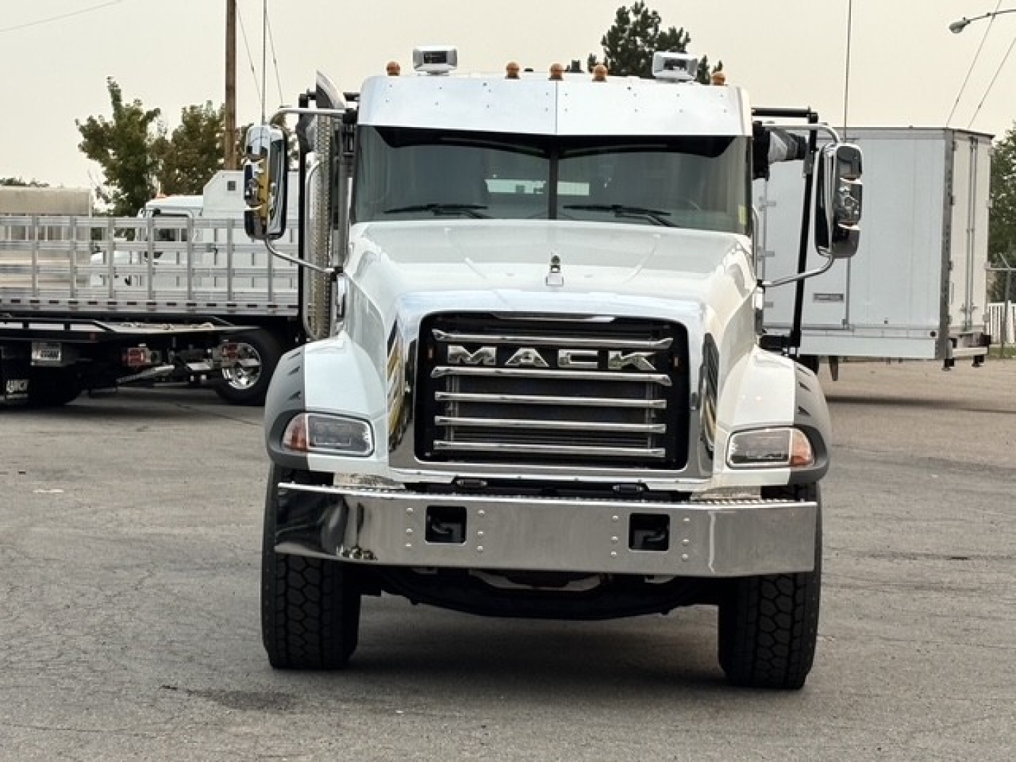 Front view of a white 2026 Mack GR64B roll-off truck with large grille and chrome bumper, Mack logo on grille, headlights, and rooftop cab lights.